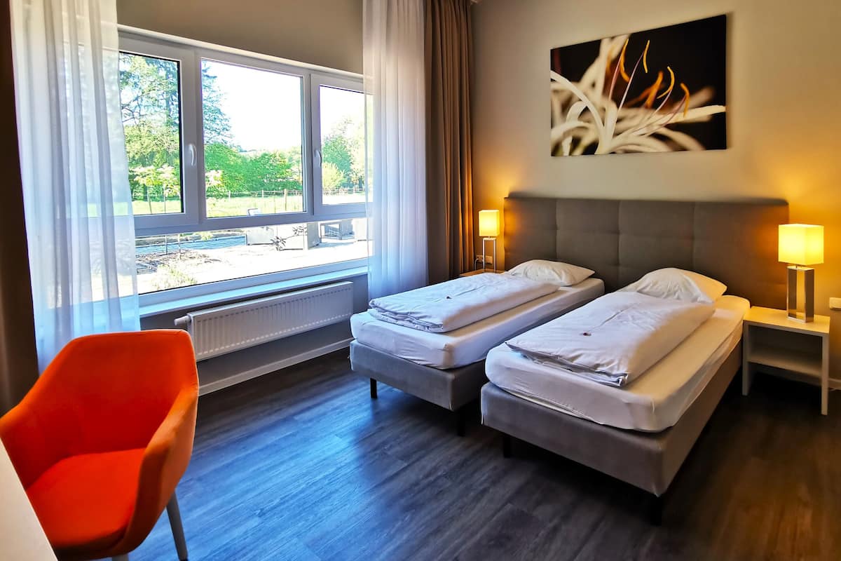 A hotel room with two beds, a bright window, a red chair, and a painting on the wall.