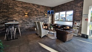 A modern interior with a brick wall, a seating area with a sofa and chairs, a small table, and a TV mounted on the wall. - Hotel Gutsmühle (Obernburg)