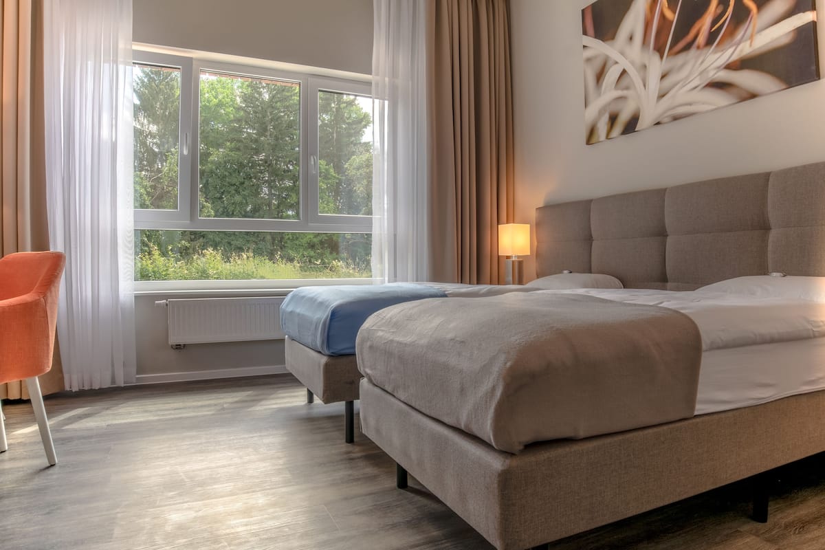 A bedroom with a bed, a chair, a window, and a lamp.