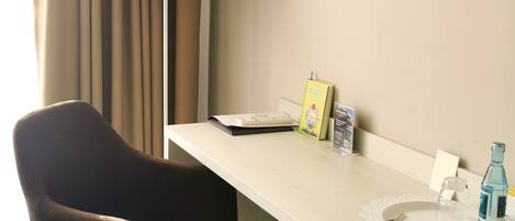 A hotel room with a desk, a chair, a TV, a lamp, and a window with curtains.