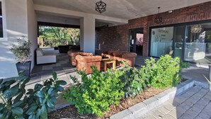 A modern outdoor seating area with a brick wall, a glass door entrance, and potted plants. - Hotel Gutsmühle (Obernburg)