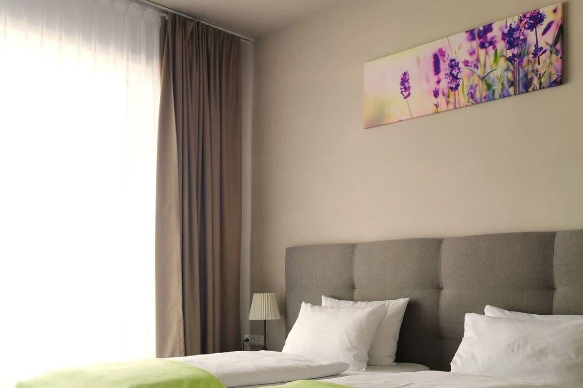 A double bed with two pillows, a bedside table with a lamp, and a painting on the wall.