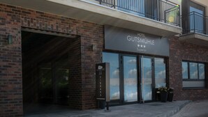 A hotel entrance with a brick facade, large glass doors, and a balcony with metal railings. - Hotel Gutsmühle (Obernburg)