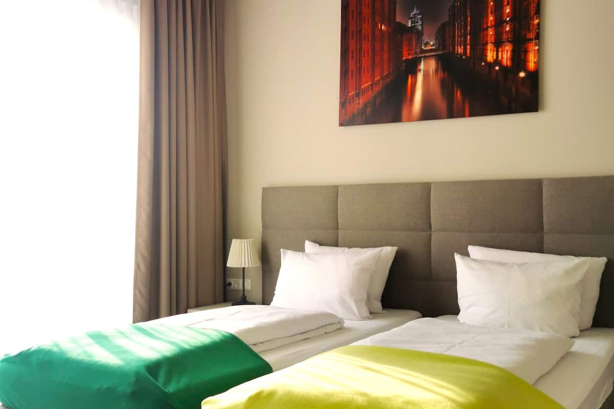A hotel room with two beds, a nightstand, a lamp, and a painting on the wall.