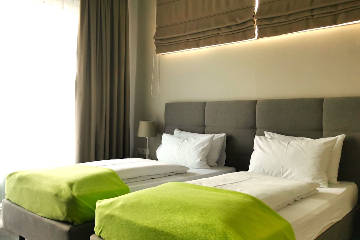 A hotel room with a large bed, two bedside tables, a lamp, and a window with curtains.