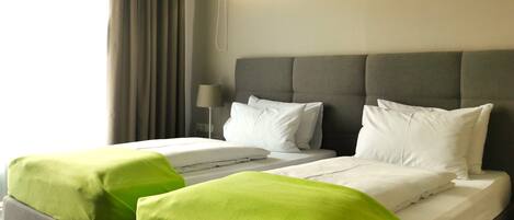 Habitación de hotel con una cama grande, dos mesitas de noche, una lámpara y una ventana con cortinas.
