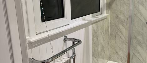 A bathroom with a shower, a window, and a radiator.