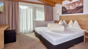 A hotel room with a wooden ceiling, a bed with white bedding, a wooden headboard, a nightstand, a desk with a chair, and a window with curtains. - Gästehaus Bergkristall (Soelden)