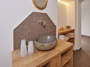 Un baño con un lavamanos de piedra, un espejo y una repisa con toallas.