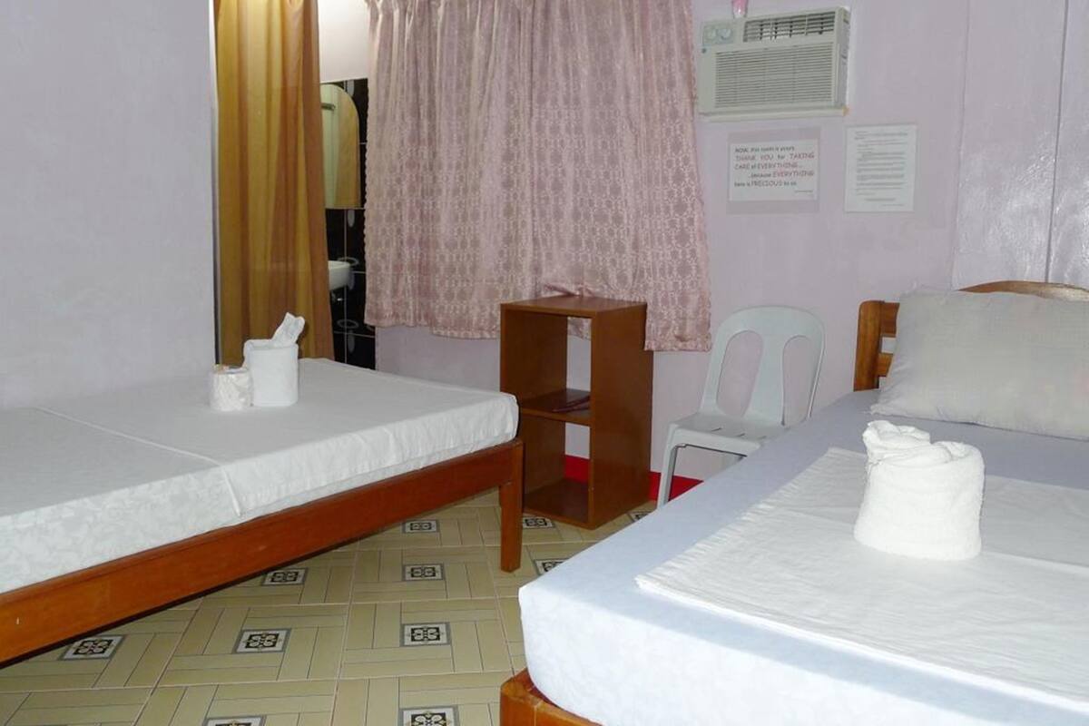 A room with two beds, a wooden chair, a small table, and a wall-mounted air conditioner.