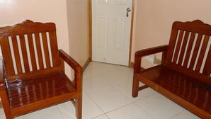 Two wooden chairs with slatted backs and armrests, positioned on a tiled floor with a white door in the background. - Amos Digue Pension House (Puerto Princesa)