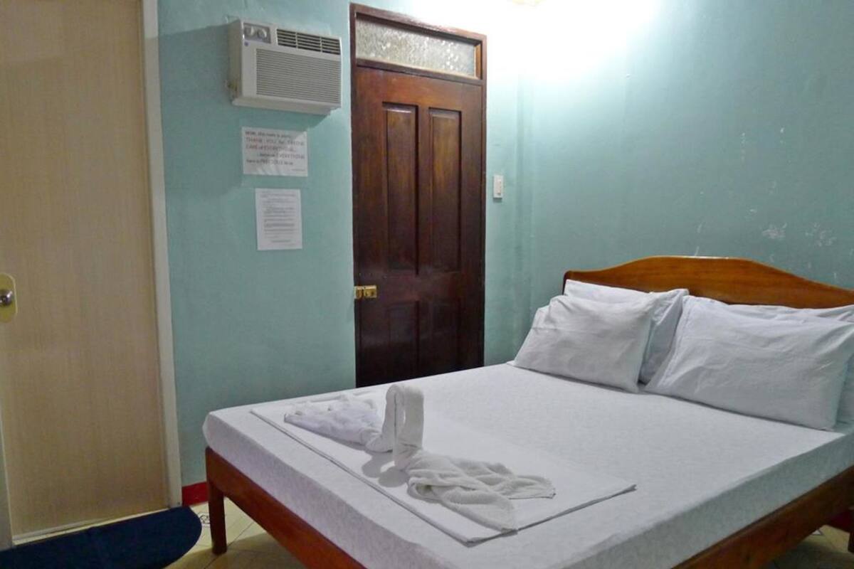 A single bed with white linens, a wooden headboard, and a white towel on the bed.