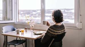 A person sitting at a table with a cup, a plate with food, and a vase with flowers. - Hlíð Bed and Breakfast (Myvatn)