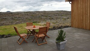 An outdoor patio with a wooden table and chairs, a potted plant, and a view of a rocky landscape. - Hlíð Bed and Breakfast (Myvatn)