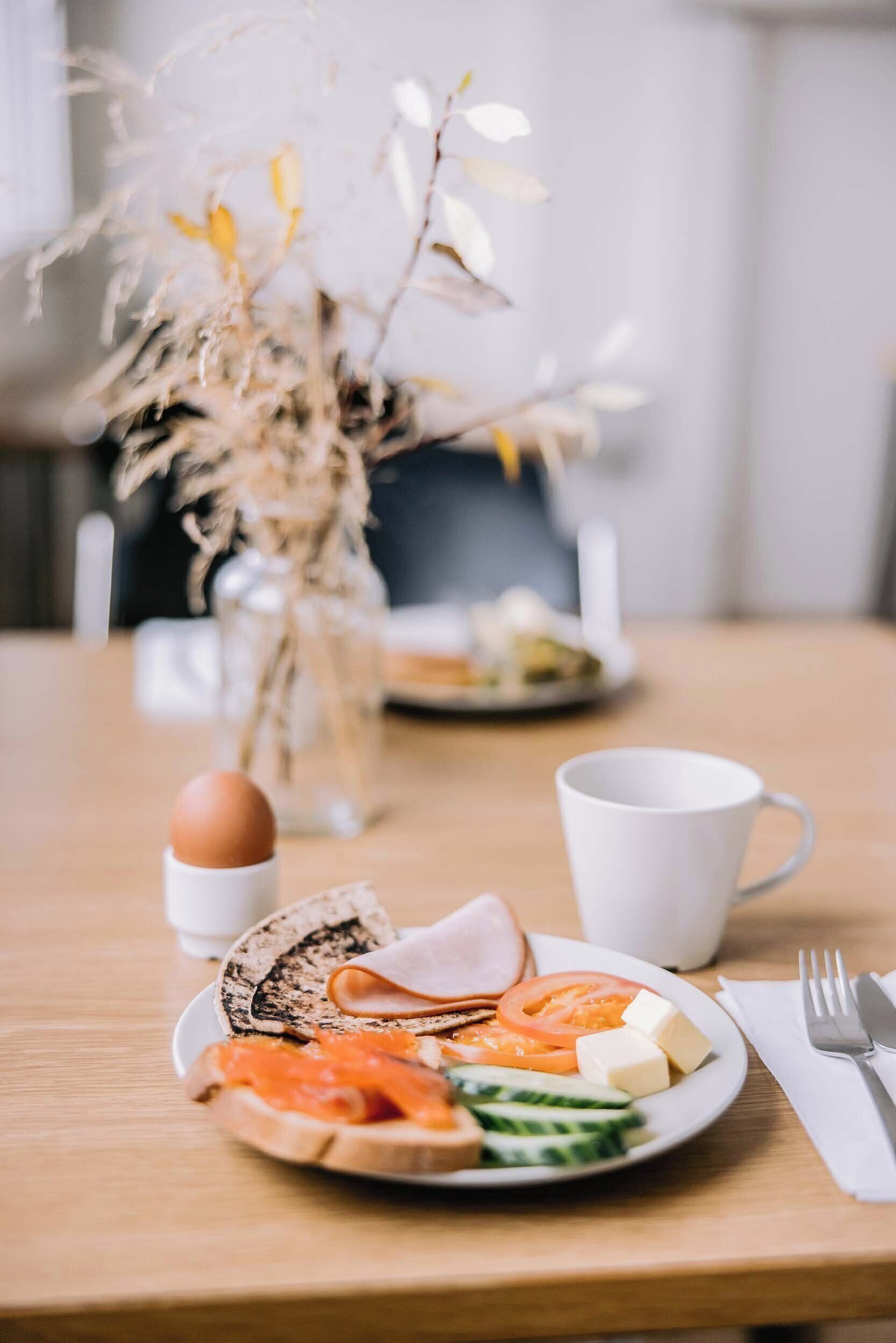 A breakfast setting with a plate of toast, ham, cheese, and vegetables, a cup, and a fork on a wooden table.