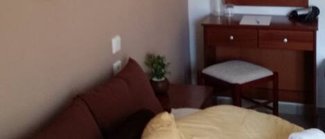 A hotel room with a bed, a bedside table with a lamp, a mirror, and a wall-mounted light fixture.