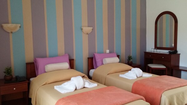 A hotel room with two beds, striped wallpaper, a wooden dresser, and a mirror.