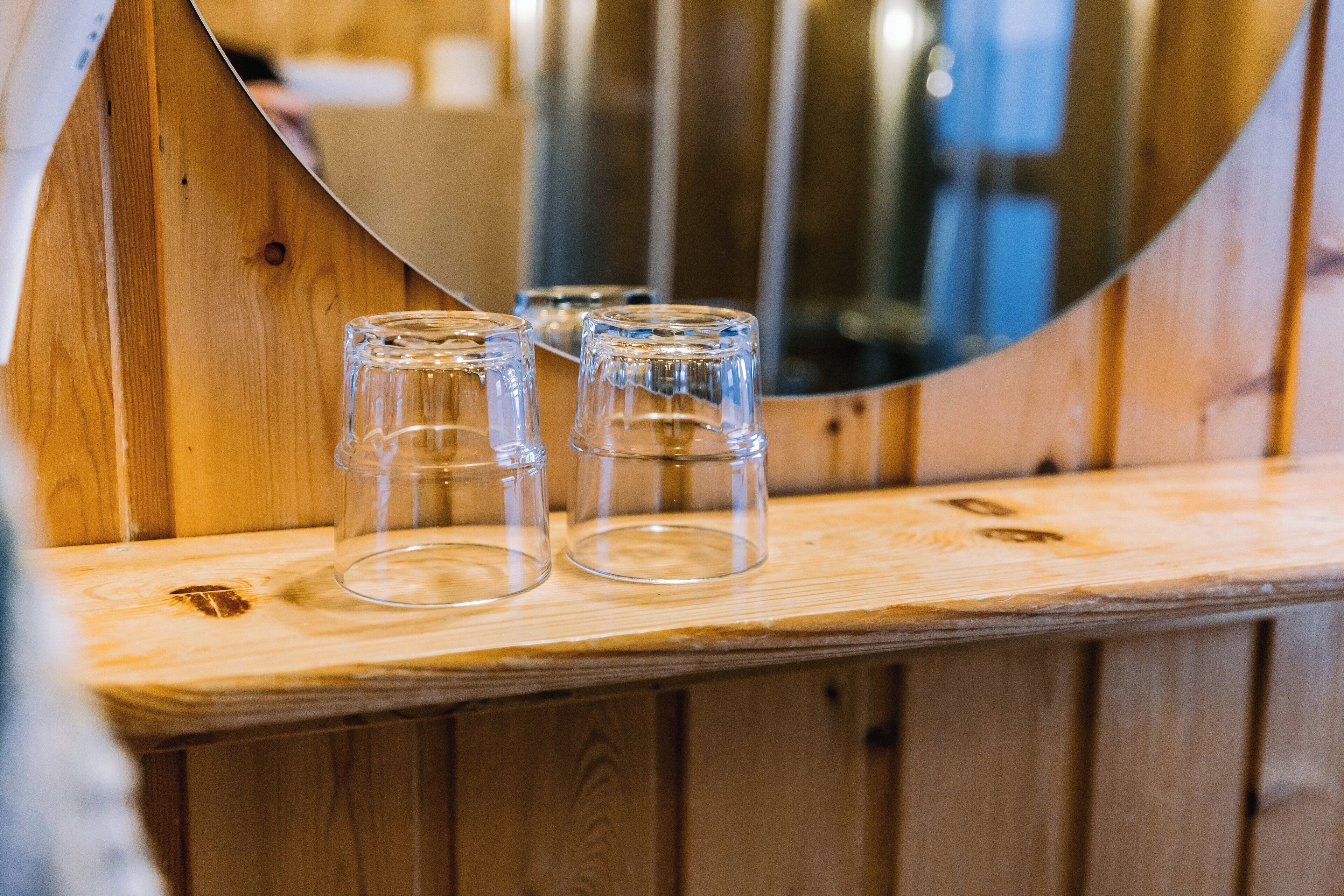 Tres vasos de vidrio transparentes sobre una superficie de madera, con un espejo curvo al fondo.