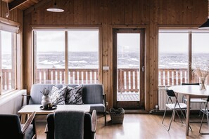 Una habitación acogedora con detalles de madera, un sofá, una mesa de comedor y ventanas amplias que dan a un paisaje nevado.