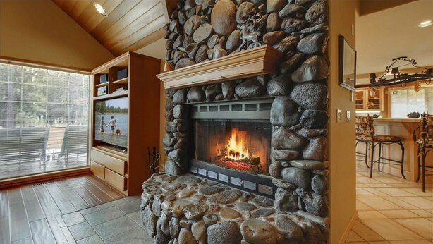 A stone fireplace with a fire, wooden shelves, a dining area with a bar, and a view through large windows. - 6 Mt. Hood-Sunriver, Oregon: Hot Tub, BBQ, WiFi, SHARC Aquatics, Tubing Hill, Mt. Bachelor, Golf, Deschutes River, Tennis, Bike Paths (Sunriver)