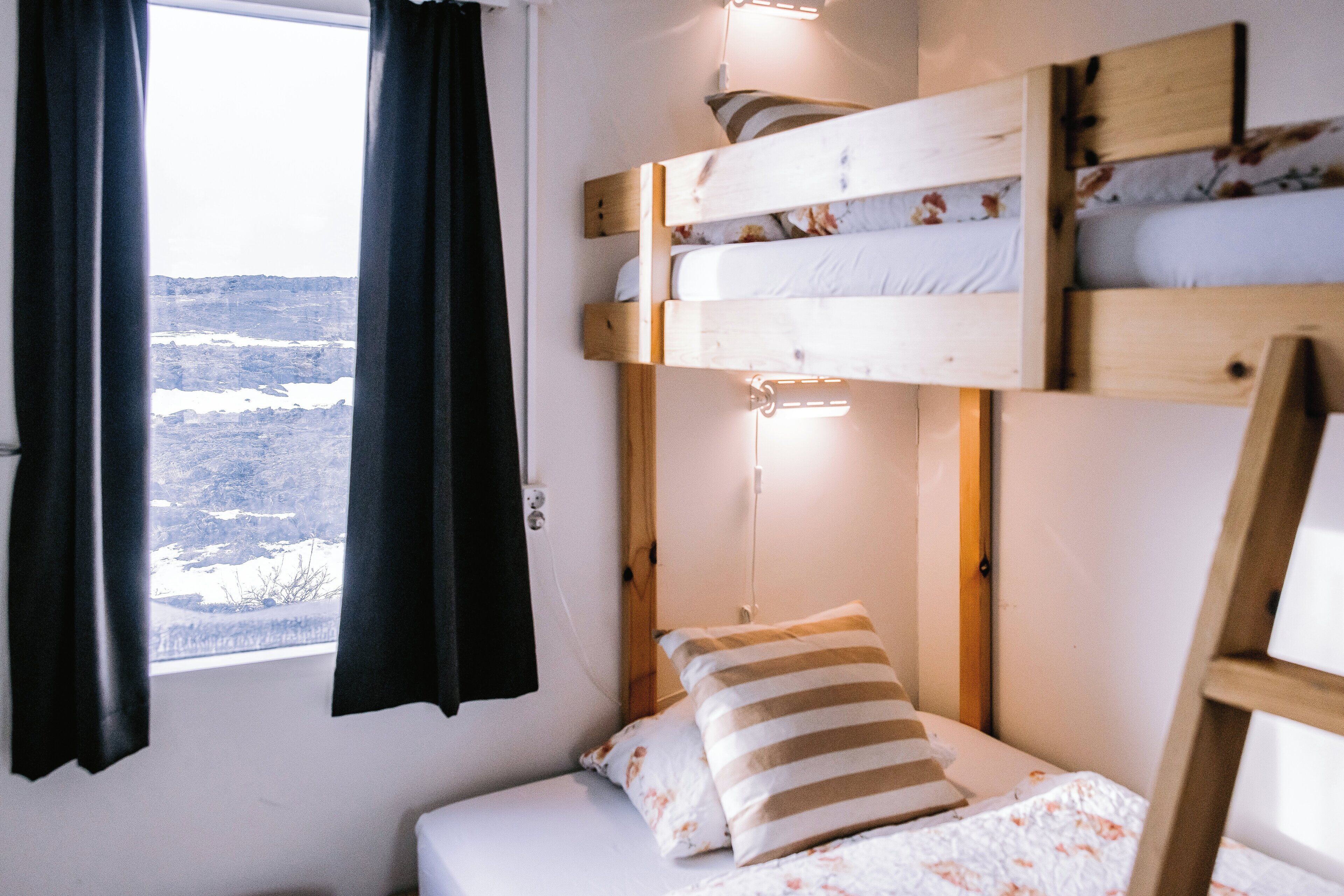 A bunk bed room with a window, curtains, and a wooden ladder.