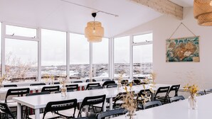 A spacious dining area with large windows, white tables, and black chairs. - Hlíd Hostel (Myvatn)