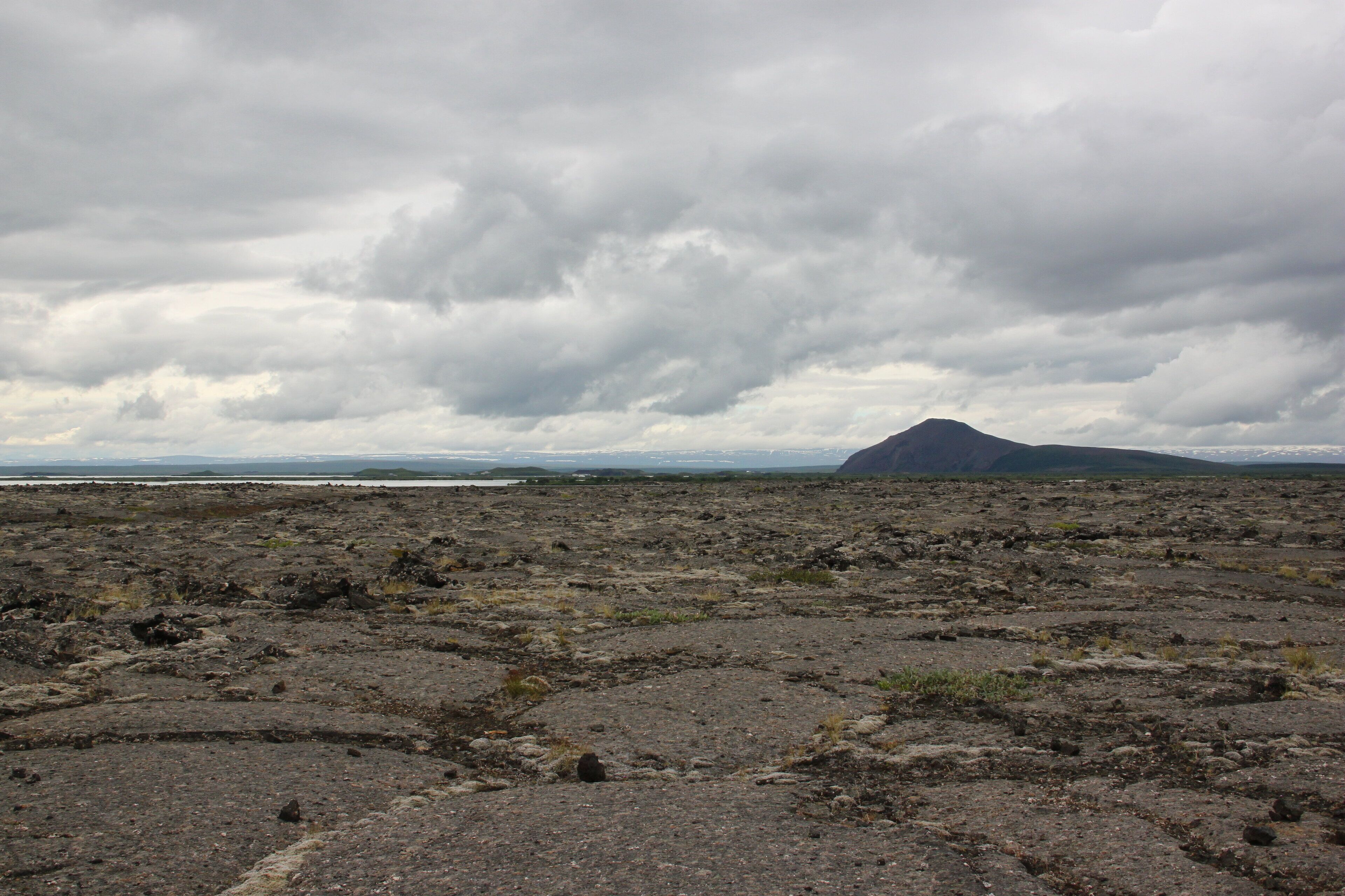 A barren landscape with a mountain in the distance under a cloudy sky.