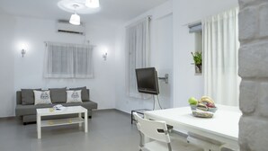 A modern living room with a white sofa, a white coffee table, a dining table with chairs, a flat-screen TV, and a window with curtains. - 2Rooms Perfect Location  1Min to  Beach (Tel Aviv)