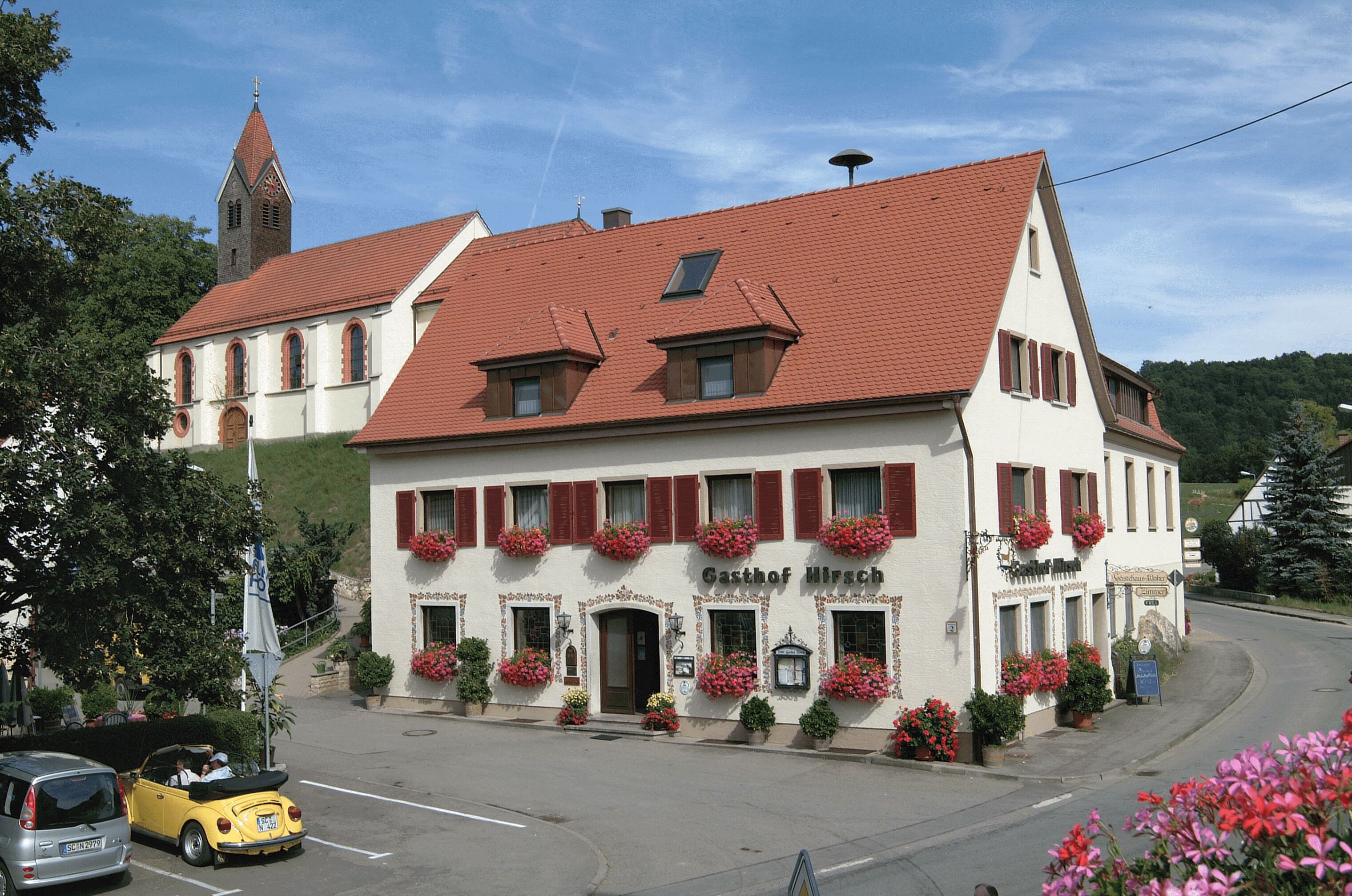 A traditional building with a red-tiled roof, arched windows, and flower boxes on the facade.