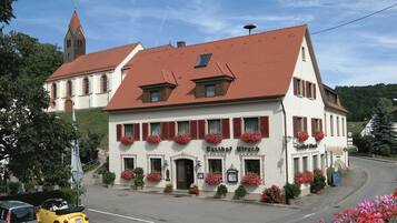 A traditional building with a red-tiled roof, arched windows, and flower boxes on the facade.