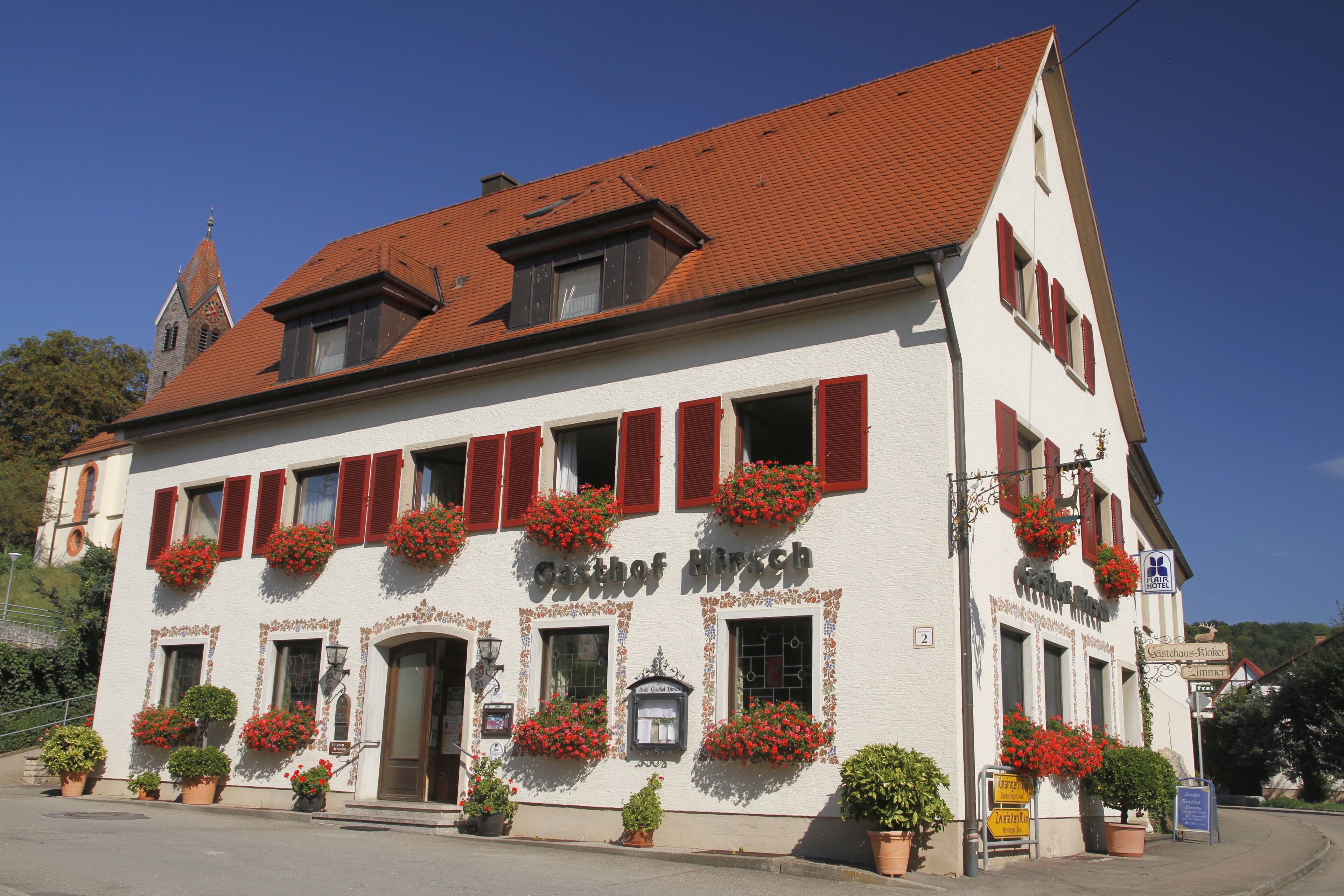 A white building with red shutters and flower boxes, labeled "Gasthof Hirsch."