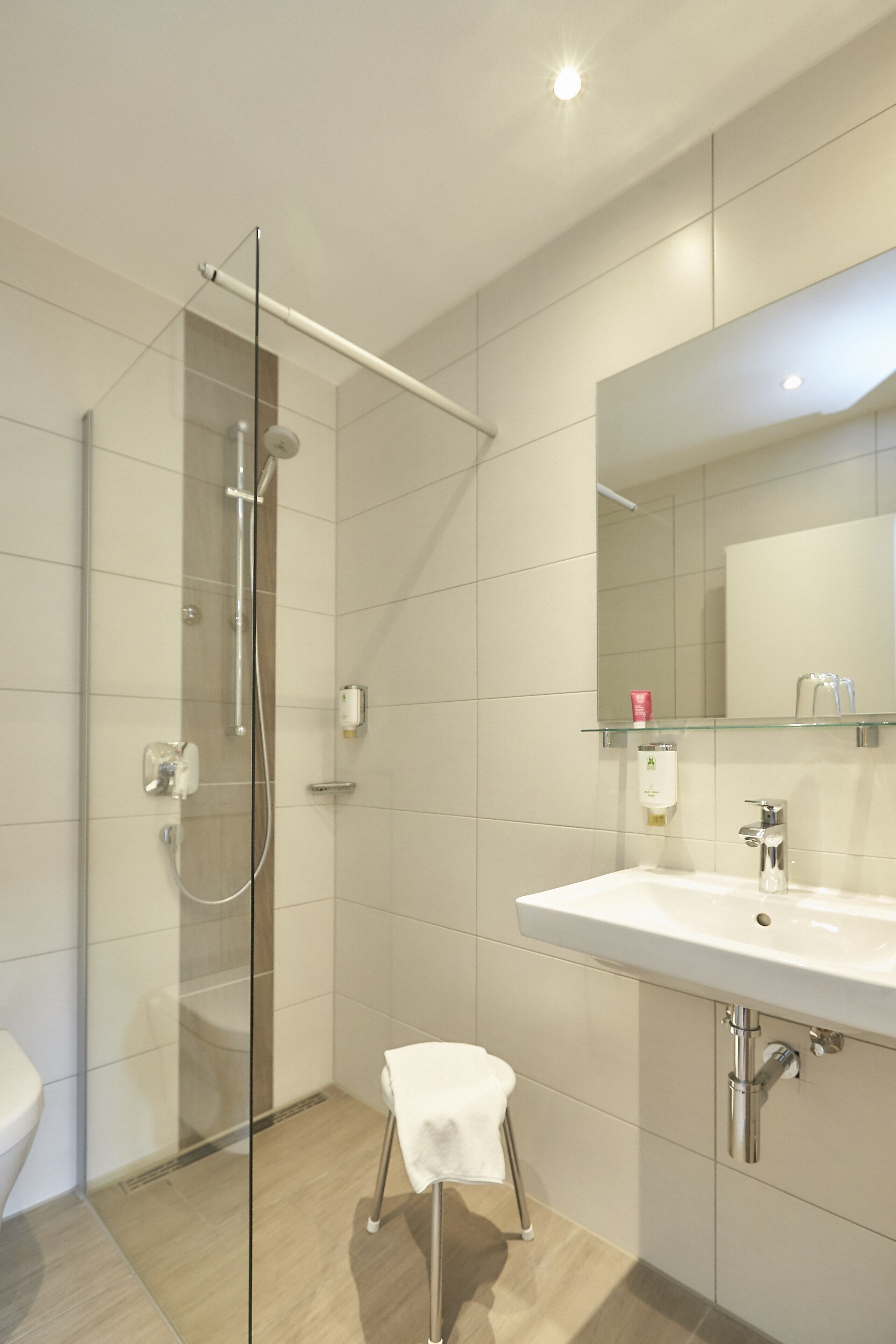 A modern bathroom with a glass shower enclosure, a white sink, and a small stool.