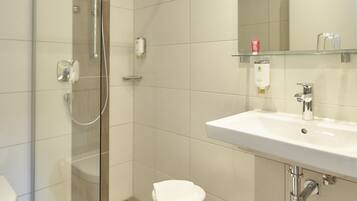 A modern bathroom with a glass shower enclosure, a white sink, and a small stool.