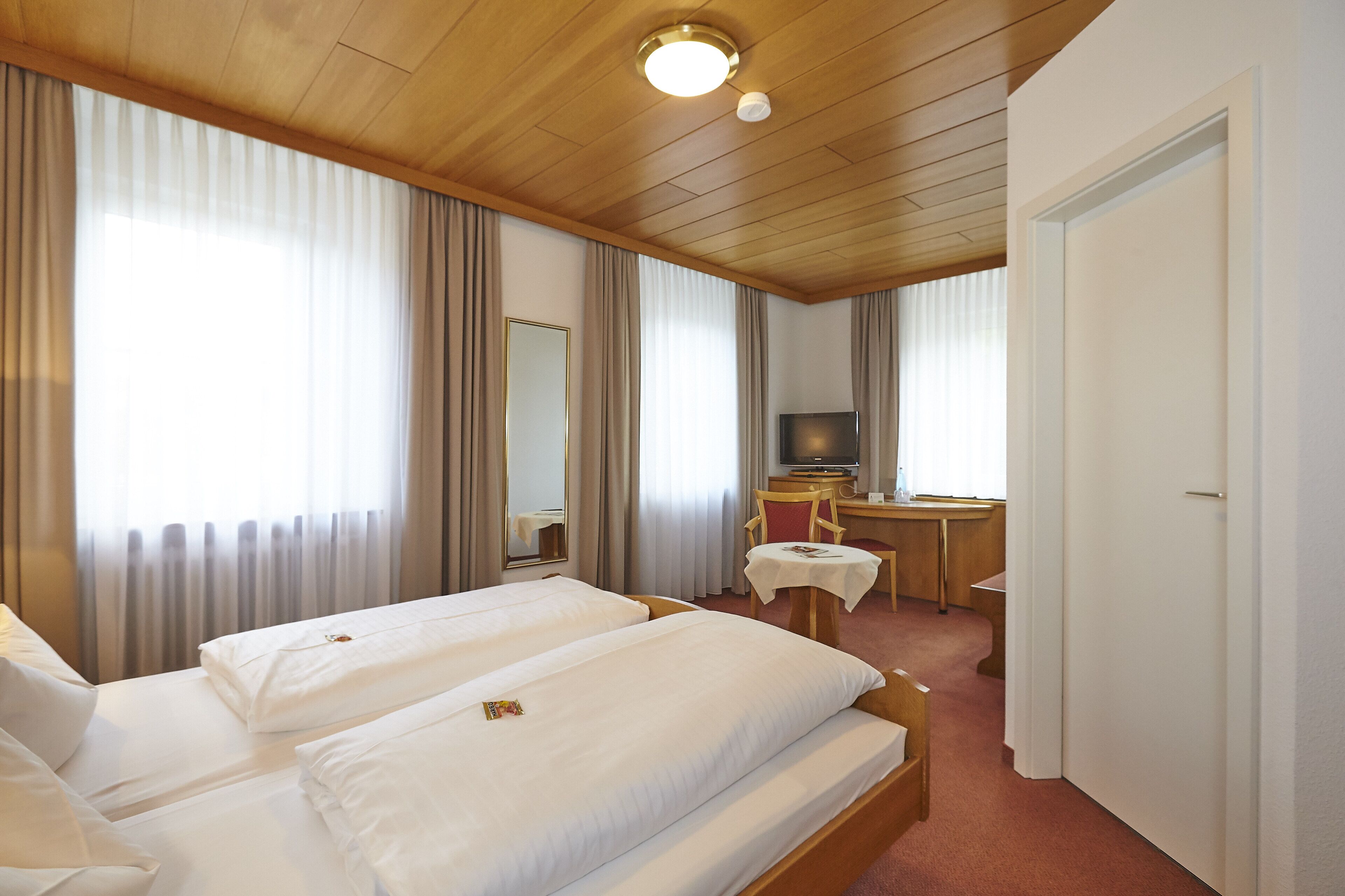 Habitación de hotel con dos camas, un escritorio, un televisor y un espejo.
