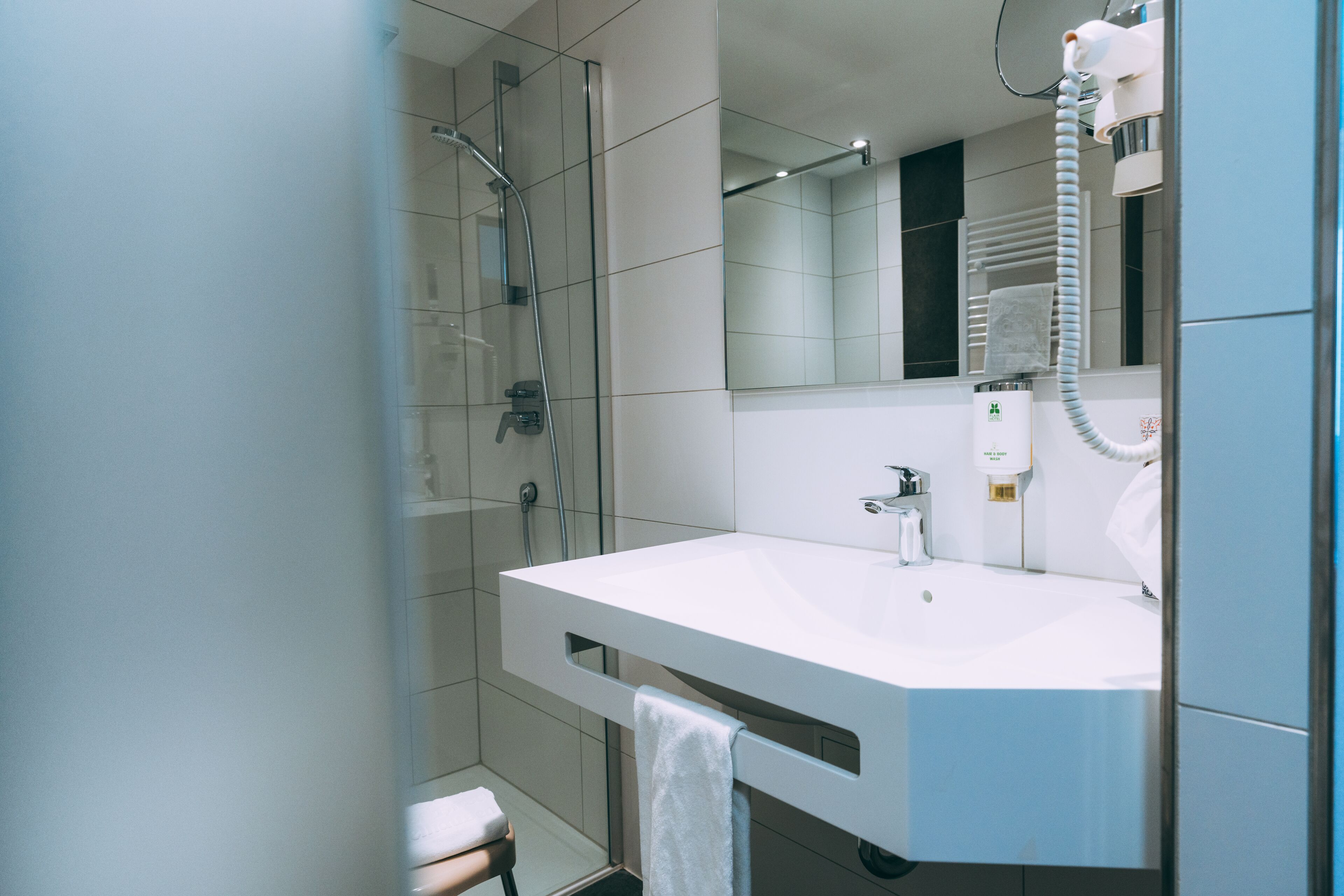 Une salle de bain moderne avec une douche à parois de verre, un lavabo blanc et une serviette accrochée au mur.
