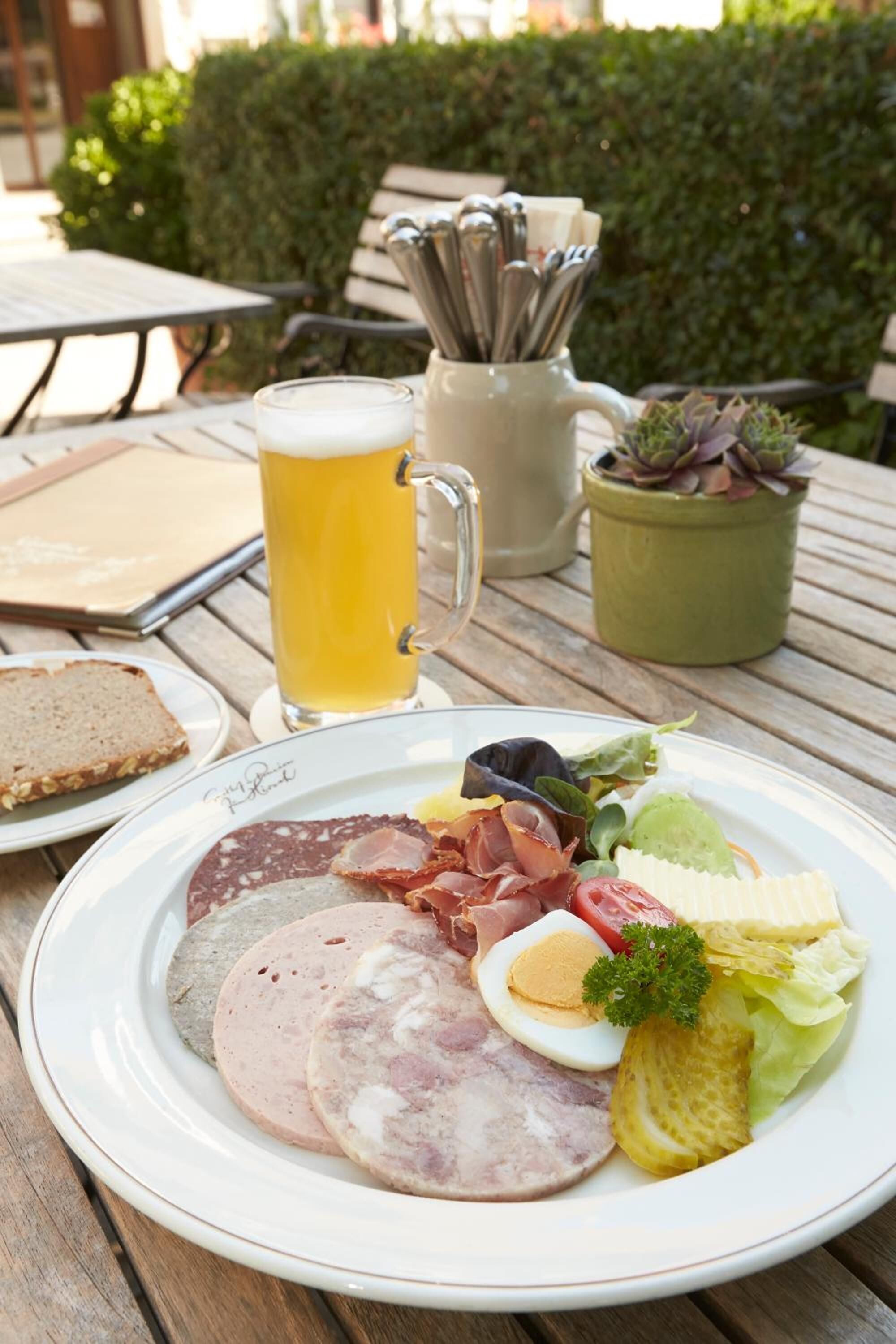 A plate of assorted meats, a boiled egg, and pickles on a wooden table.