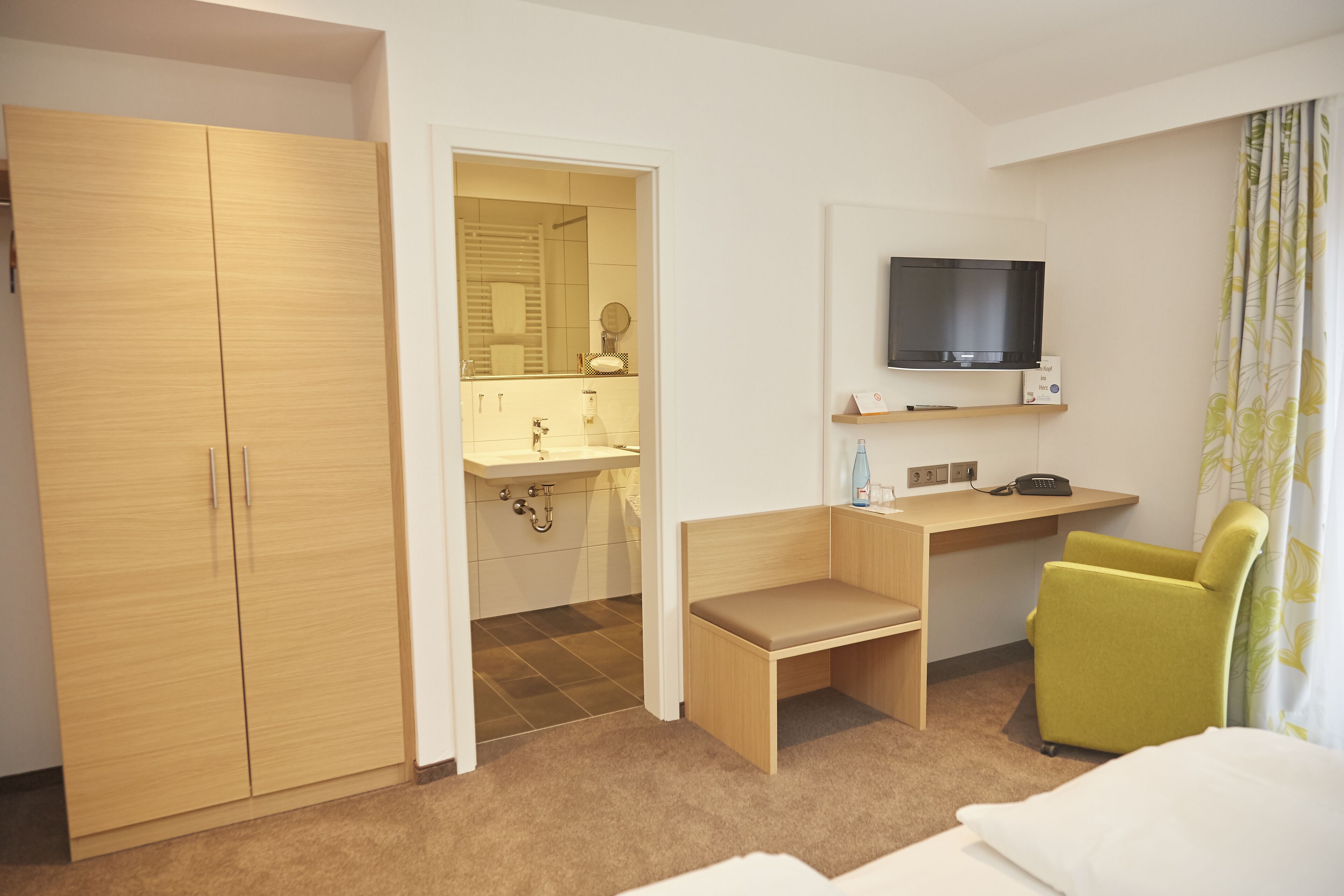 Une chambre d’hôtel comprenant un placard, une salle de bain avec un lavabo et un miroir, un bureau avec une chaise, une télévision et un lit.