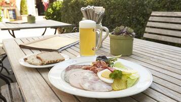 Un repas composé de pain, de jambon, d’œufs et de salade, servi sur une table en bois à l’extérieur.