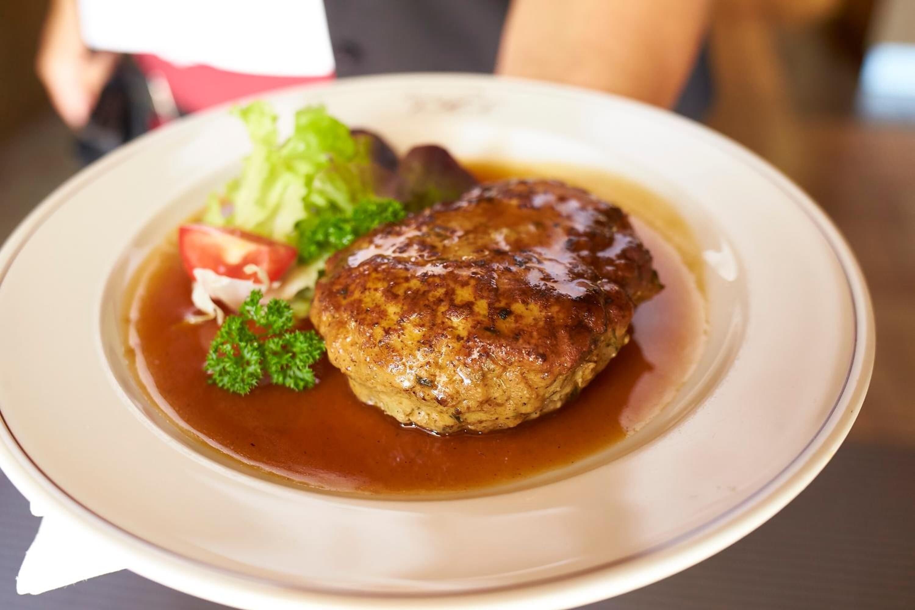 A plate with a meat patty, vegetables, and sauce.