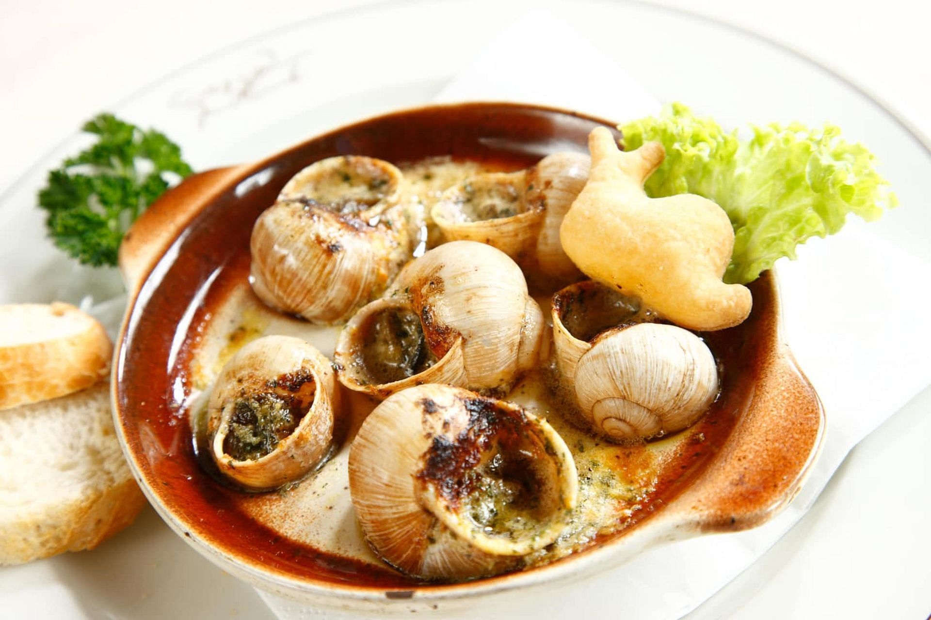 A dish of escargot served in a brown bowl with a side of bread and a garnish of parsley.