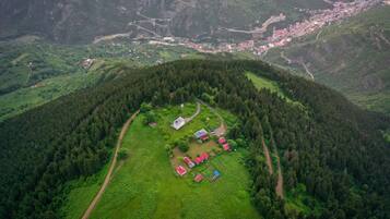 An aerial view of a mountainous village with a cluster of red-roofed buildings surrounded by dense forests.