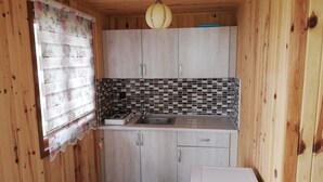 Une cuisine compacte aux murs en bois, avec un pare-feu en carrelage, une cuisinière à gaz, un évier et un réfrigérateur blanc.