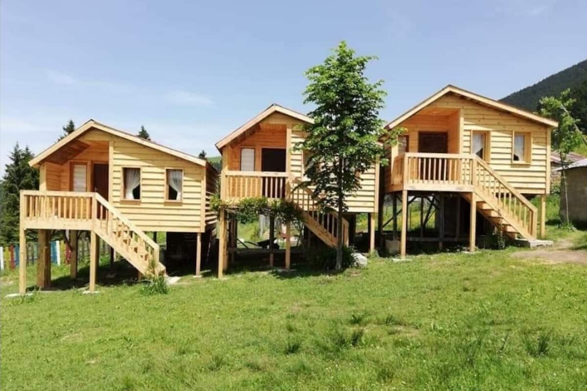 Een rij houten chalets met balkons en trappen, gelegen in een grasrijk gebied met een berg op de achtergrond.