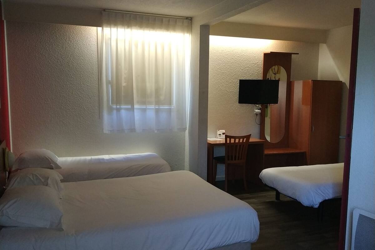 A hotel room with two beds, a desk, a chair, a television, and a clock on the wall.