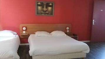 A hotel room with a large bed, two bedside tables, a nightstand, and a red wall with a framed artwork.
