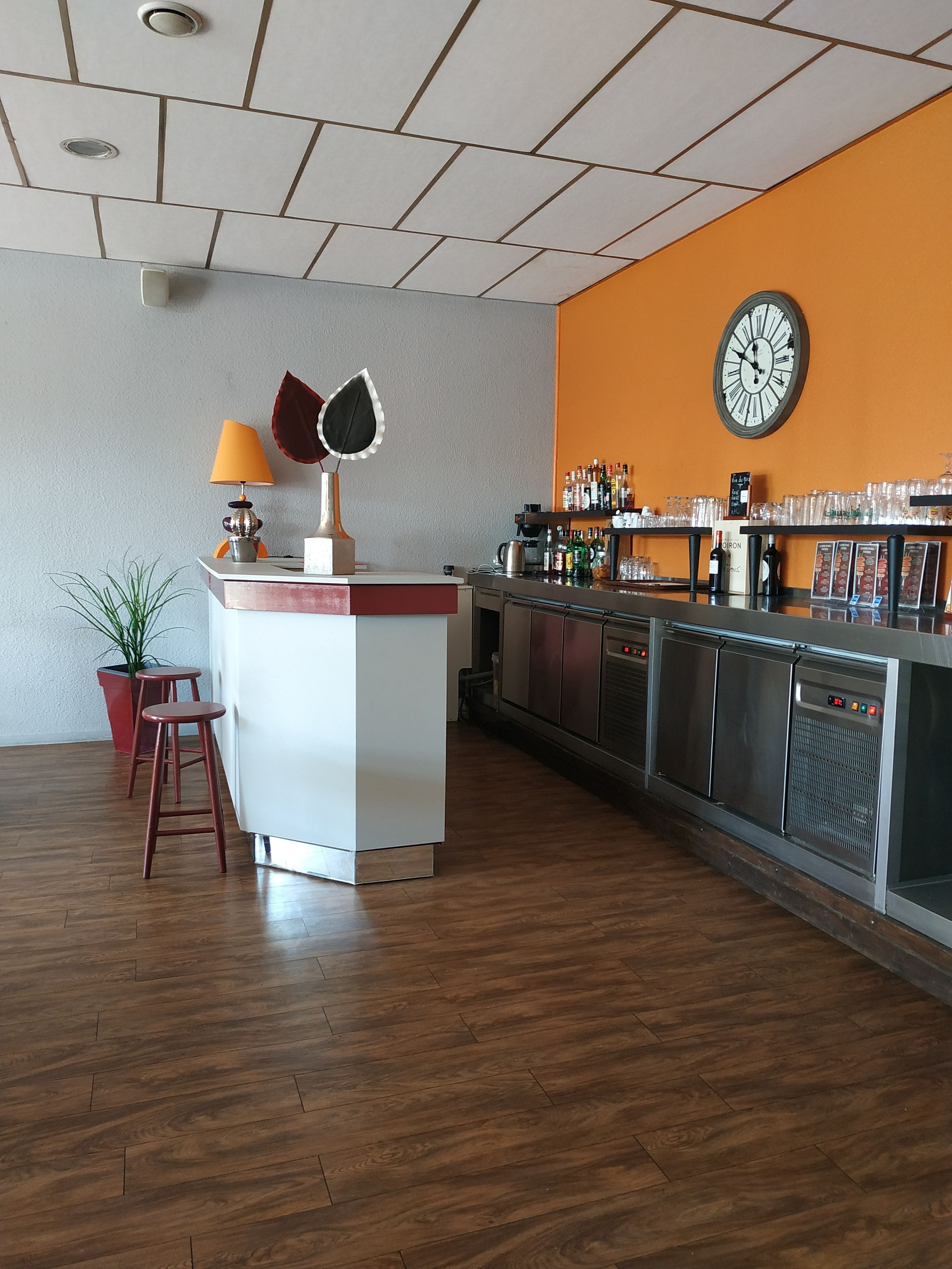 A bar area with a wooden floor, a white counter, and a clock on the wall.