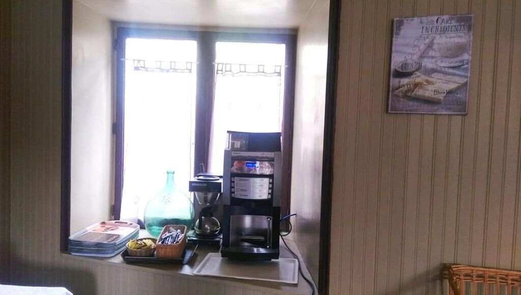 Uma cozinha com cafeteira, janela com cortinas e um pôster na parede.