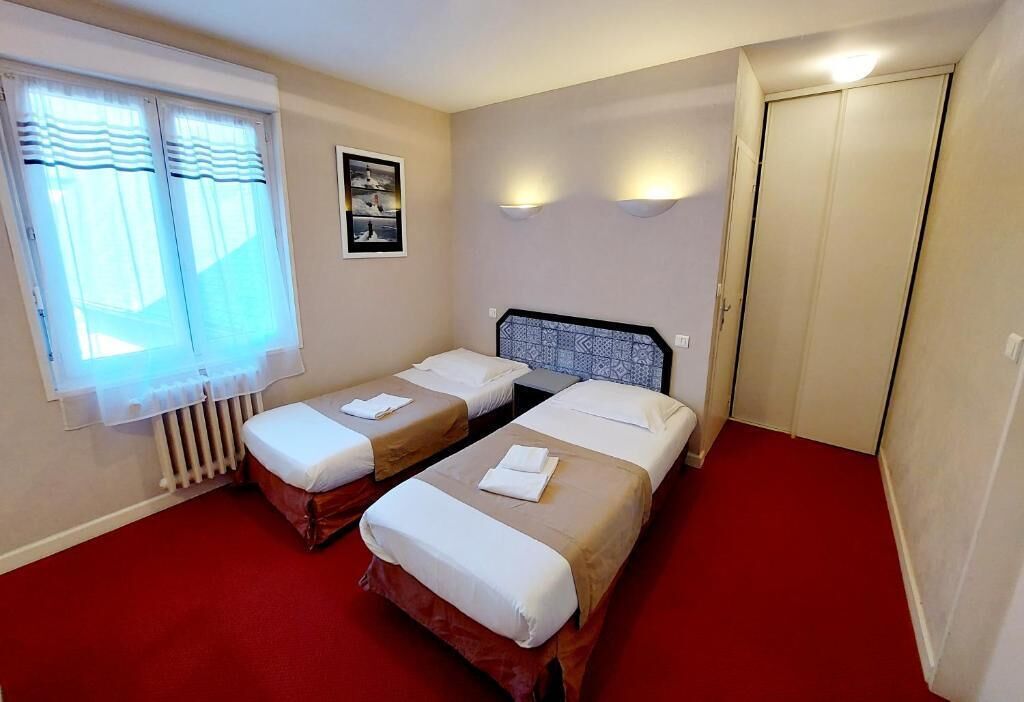 A hotel room with two single beds, a radiator, a window with curtains, a wall-mounted picture, and a door.