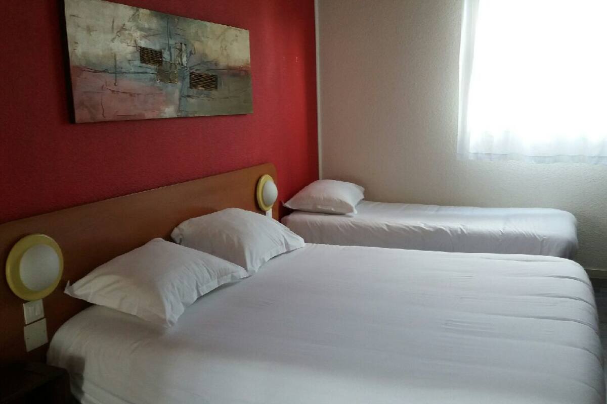 A hotel room with two beds, a red wall, and a painting.