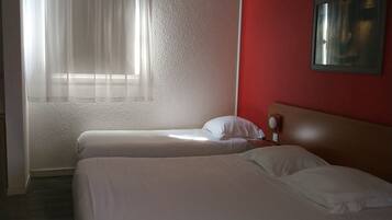 Una habitación de hotel con dos camas, una pared de acento roja, una ventana con cortinas traslúcidas y un cuadro en la pared.